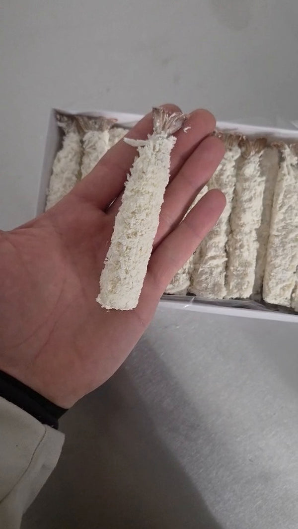 Garnelenkönig Torpedo Shrimps 26/30 paniert – Garnele in der Handfläche, dahinter die geöffnete 800-g-Packung